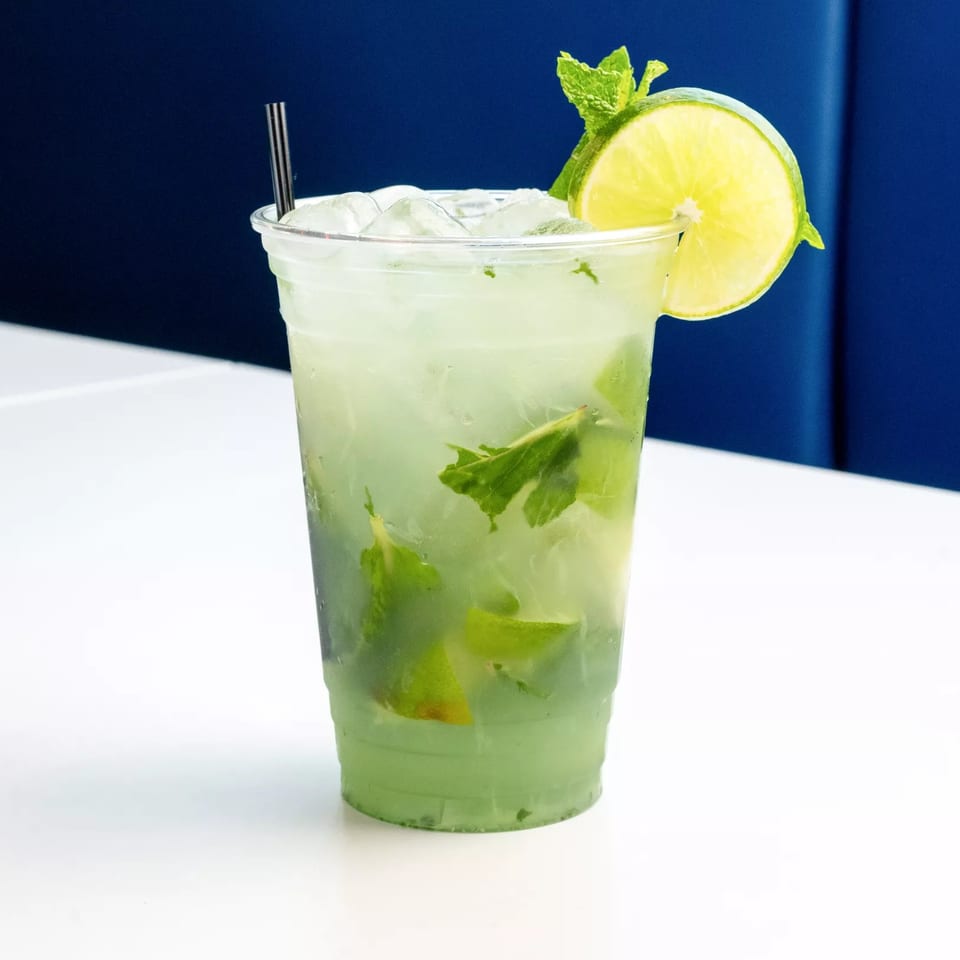 Iced mint mojito with lime wedges, lime garnish, and fresh mint in a clear cup.