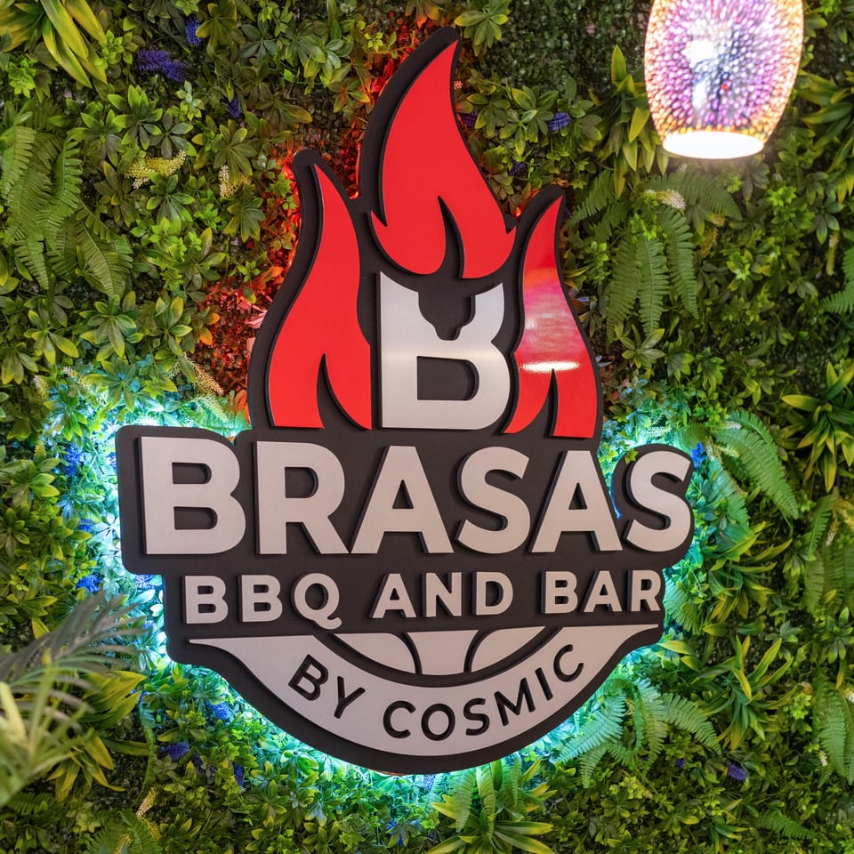 Brasas BBQ and Bar by Cosmic sign with red flames and white text on a green leafy wall.