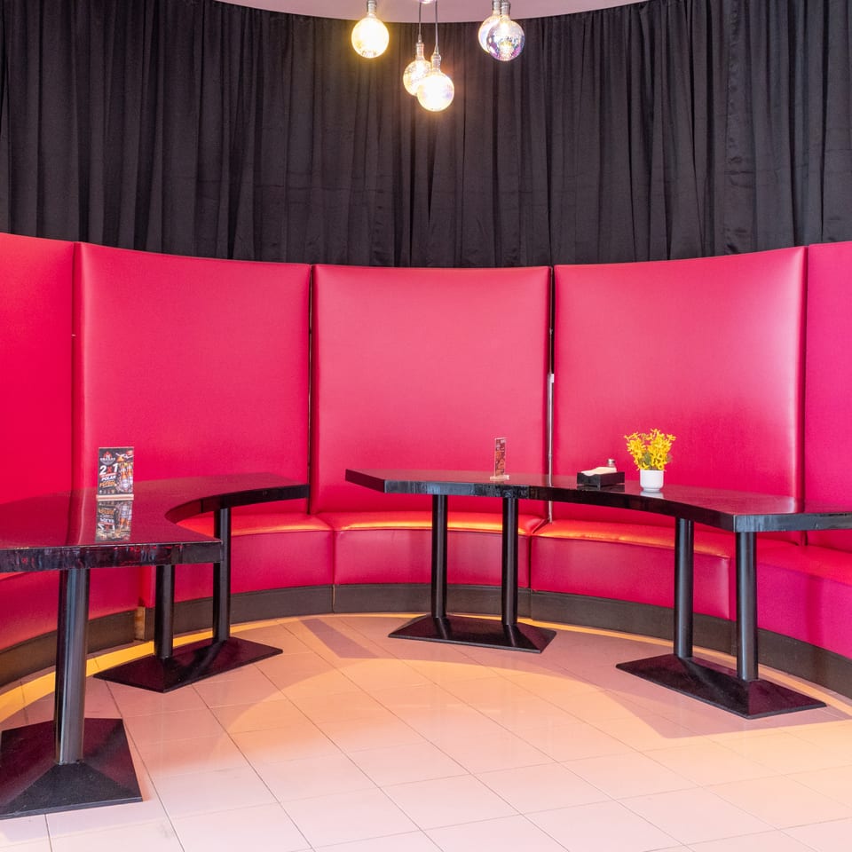 A vibrant restaurant interior with curved red booths, black tables, and a dark curtain backdrop.