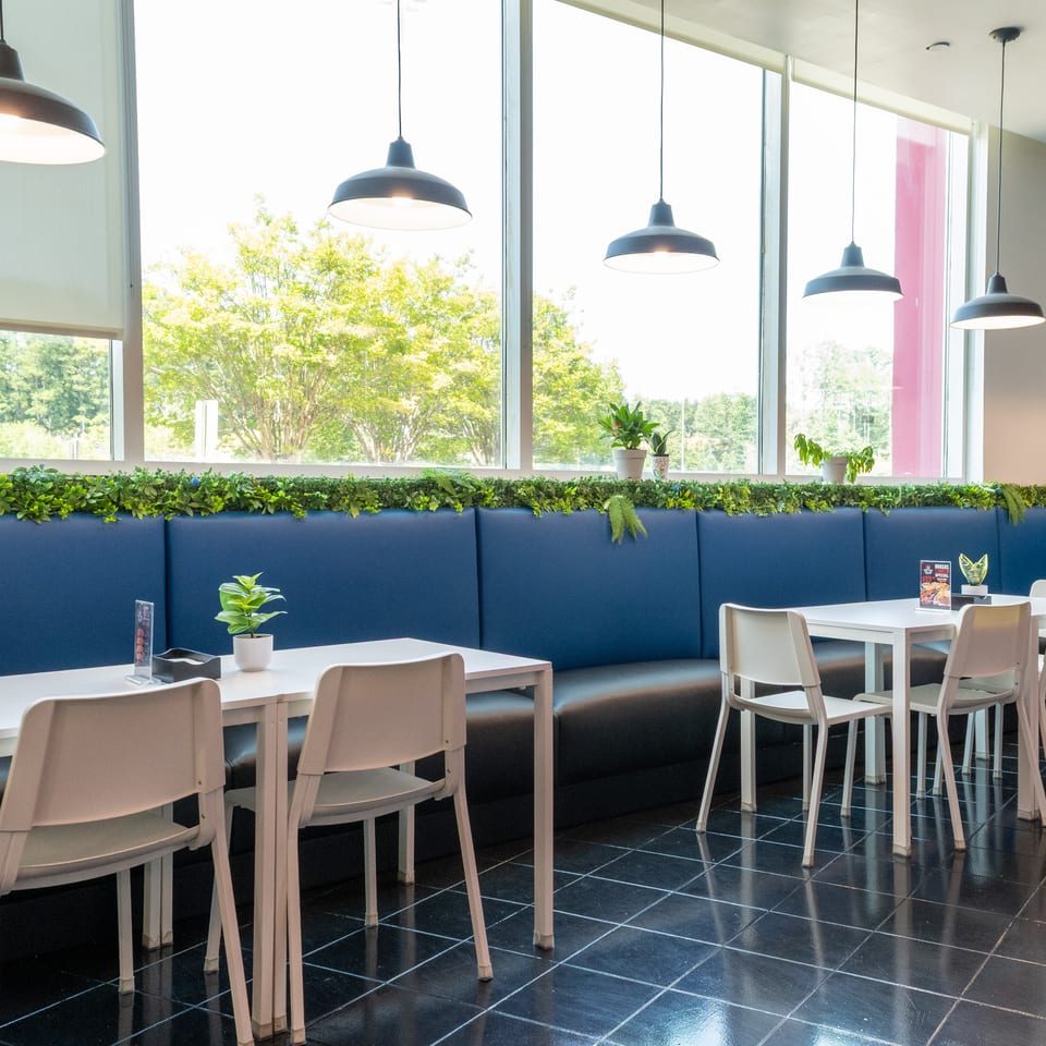 Modern restaurant interior with blue booth seating, white tables, chairs, and large windows.