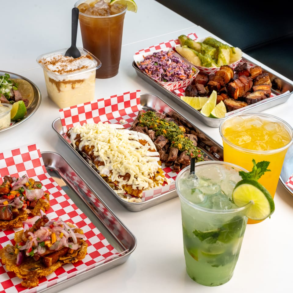 A vibrant spread of Latin American dishes and drinks, including tacos, plantains, and cocktails.
