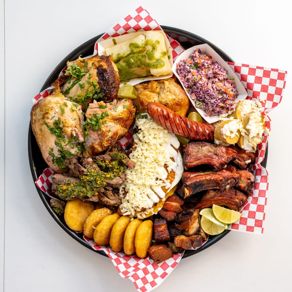 A large platter of grilled meats, including chicken, ribs, sausage, and steak, with sides.