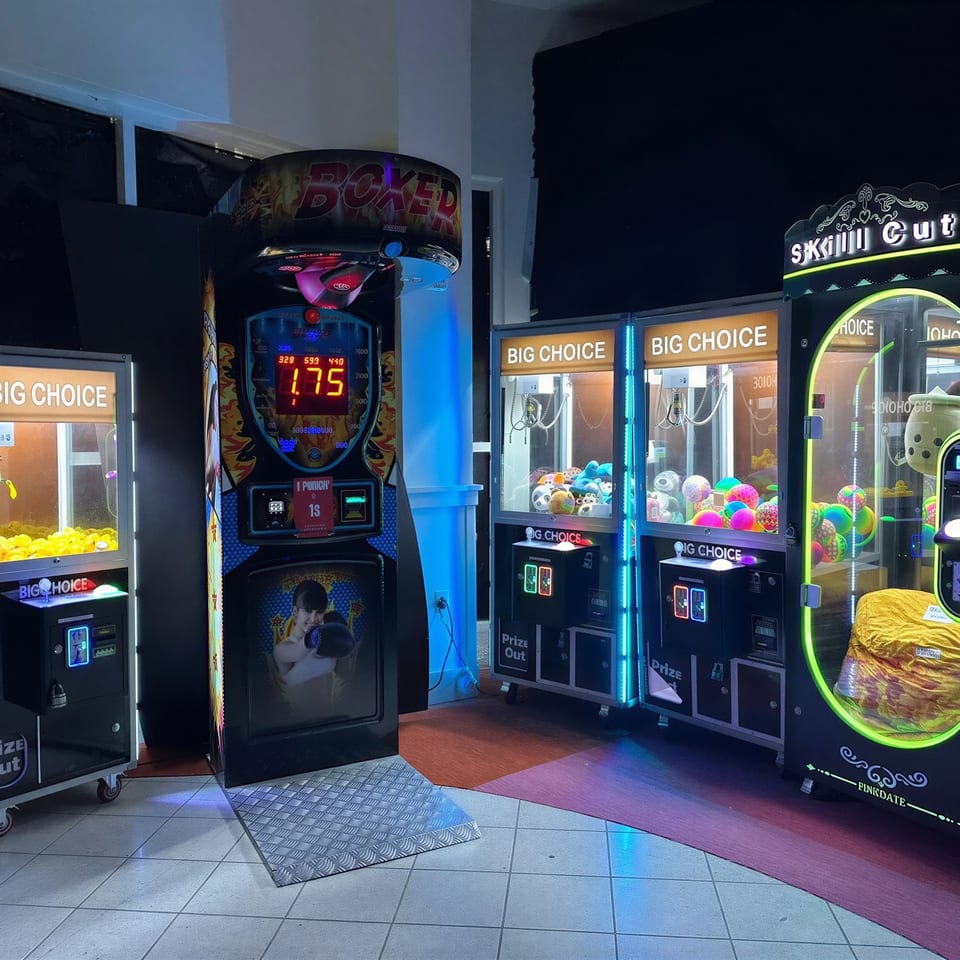 Arcade games, including claw machines with prizes and a boxing game, illuminated with neon lights.
